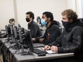 学生们戴着口罩坐在教室里的电脑前